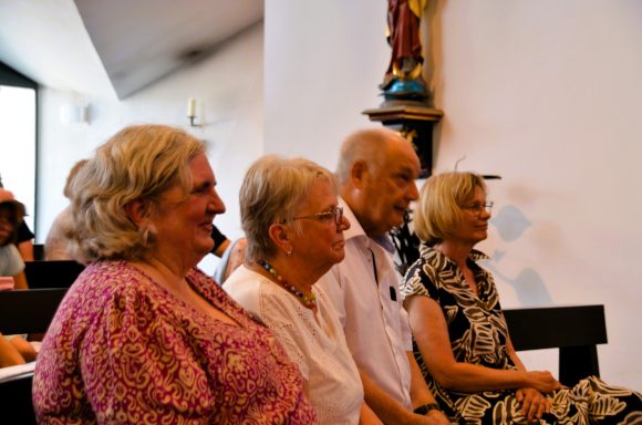 Abschiedsfeier Vier Personen sitzen in einer Kirche, erfreut, während sie dem Geschehen folgen.